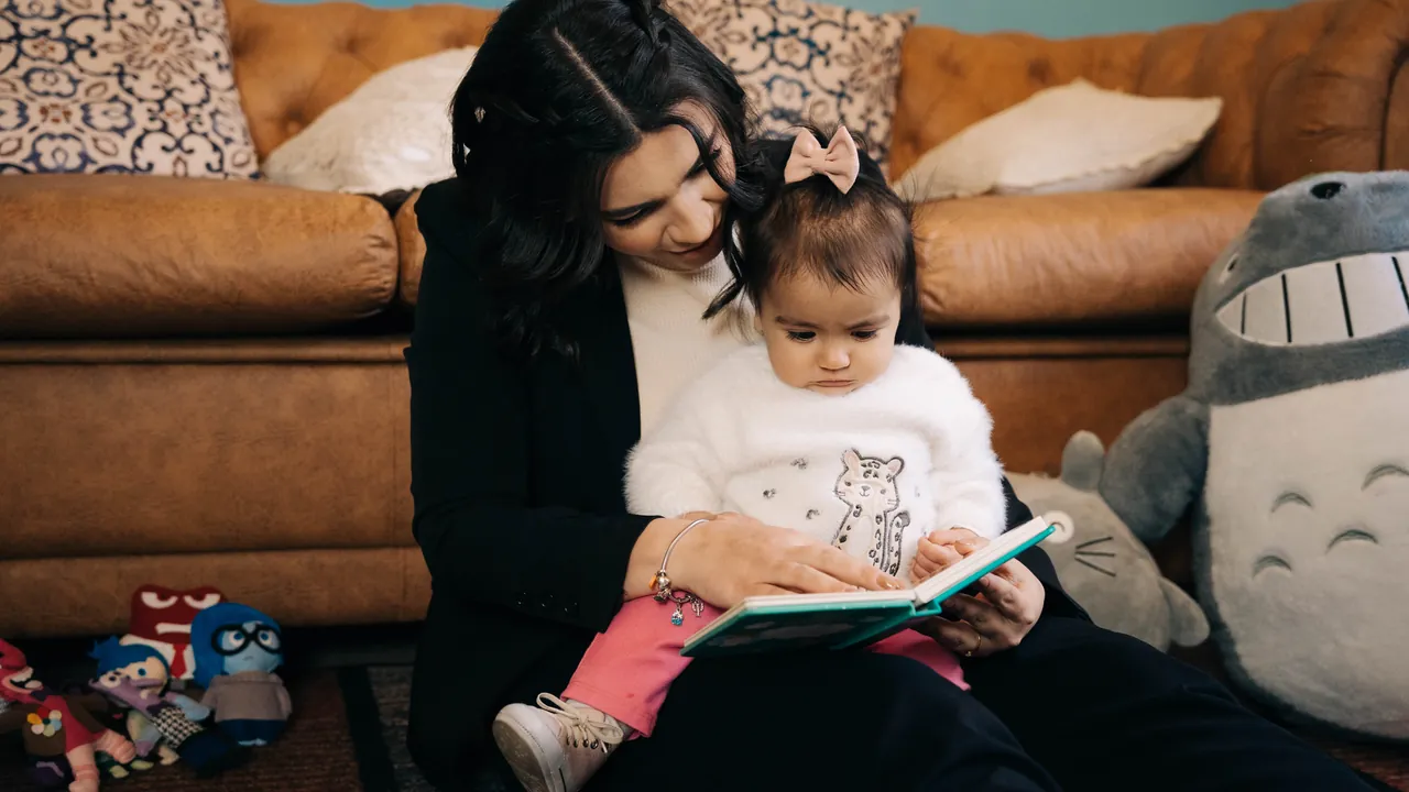 Mariana Gouvêa lendo um livro com um bebê no colo, sentados no chão