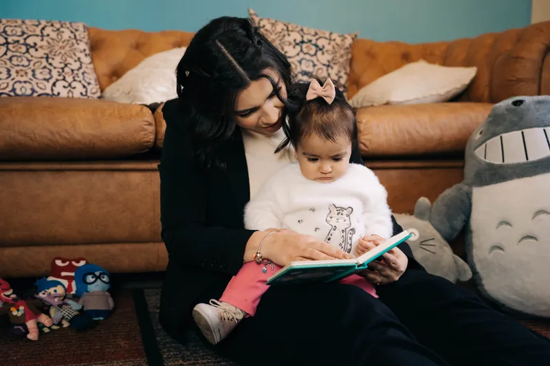 Mariana Gouvêa lendo um livro com um bebê no colo, sentados no chão
