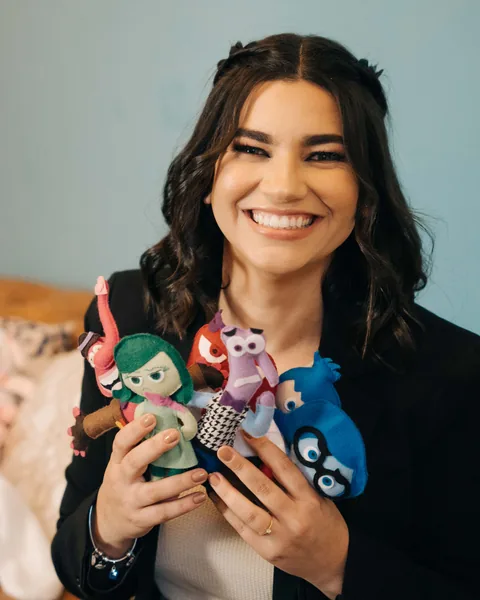 Mariana Gouvêa, psicóloga infantojuvenil, sorrindo enquanto segura bonecos do Divertidamente que representam as emoções